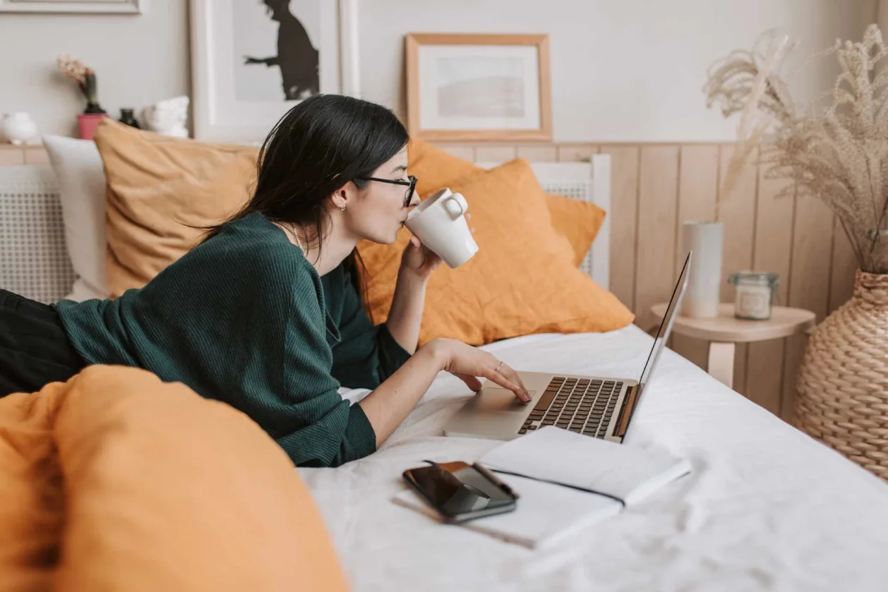woman wearing blue light glasses while working on bed